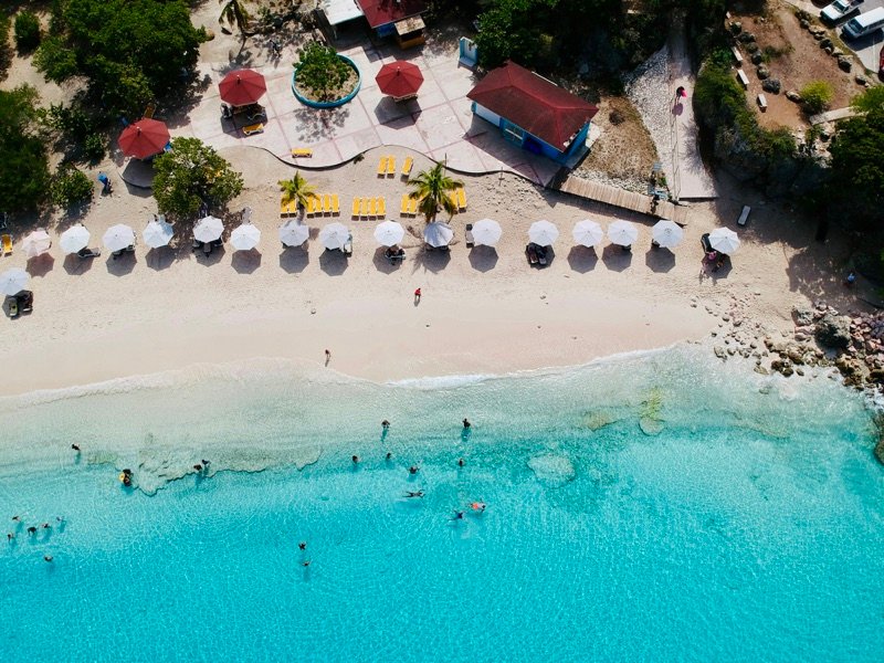 Vista aérea de una playa de arena blanca con sombrillas y agua turquesa